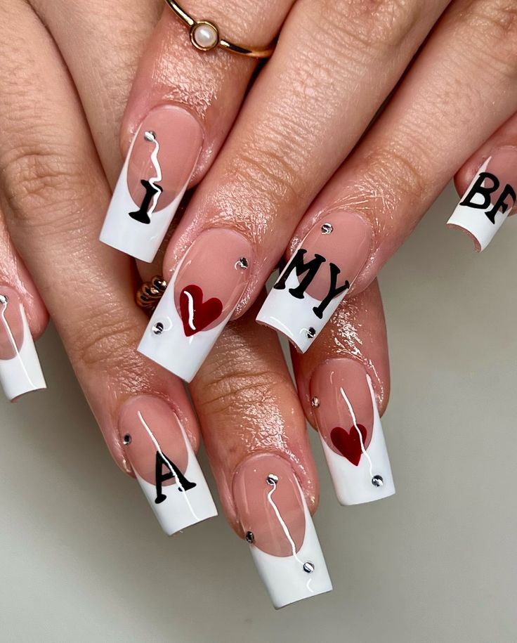 Chic French Tip Nail Design with Elegant Black Lettering, Heart Embellishments, and Glamorous Rhinestones.