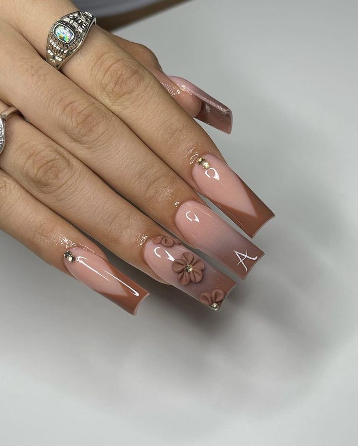 Elegant Ombre Nail Design: Soft Nude to Rich Brown with Floral Embellishments and Gems.