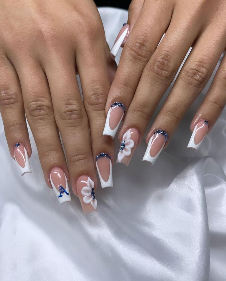 Elegant Nude and White Nail Design with Deep Blue Rhinestones and Floral Accents.