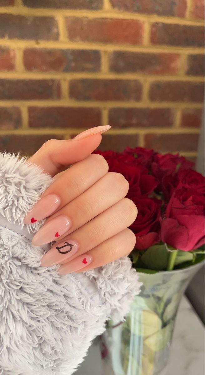 Elegant Nude Nail Design with Delicate Red Heart Accents and Pointed Tips for a Romantic Look.