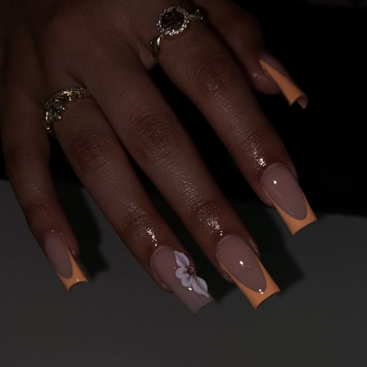 Sophisticated Nude and Orange Nail Design with Floral Accents and Dainty Rings