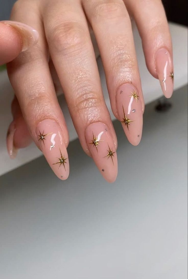 Chic Nude Nail Design with Sparkly Gold Star Accents for Glamorous Elegance.