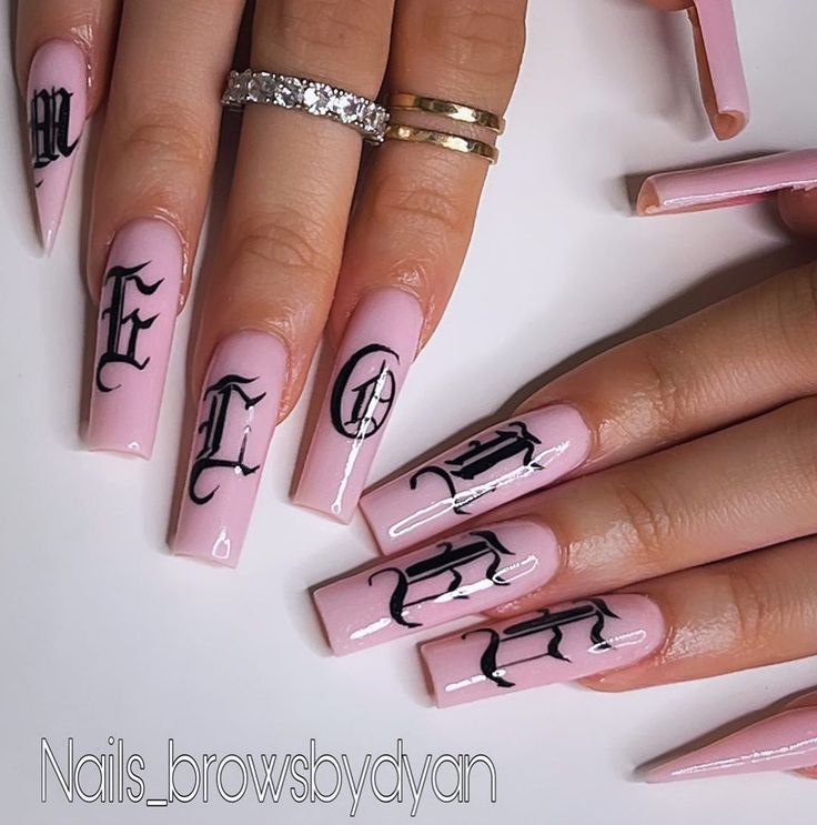 Chic Sophistication: Elegant Pink Nail Design with Intricate Black Lettering and Stylish Ring Accents.