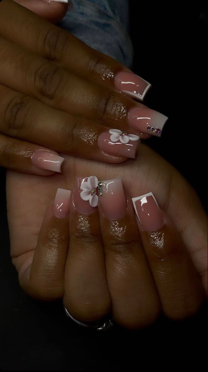 Sophisticated Nude Nail Design with Glossy Finish, Delicate Tips, 3D Floral Embellishments, and Rhinestone Accents.