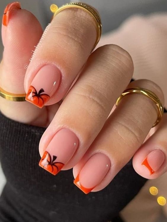 Stylish Nude Nail Design Accented with Vibrant Orange Tips and Playful Black Bow Details