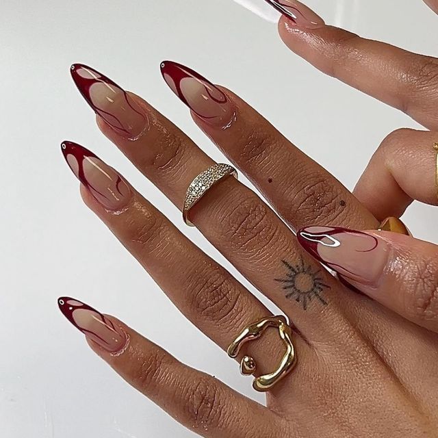 Chic Stiletto Nail Art in Nude and Deep Red with Intricate Swirls and Glossy Finish.