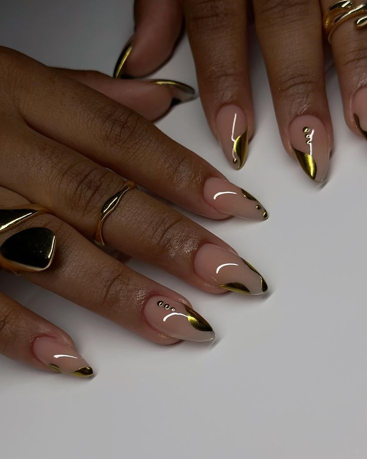 Chic Stiletto Nail Design: Nude Base with Gleaming Gold Accents and Sophisticated Embellishments.