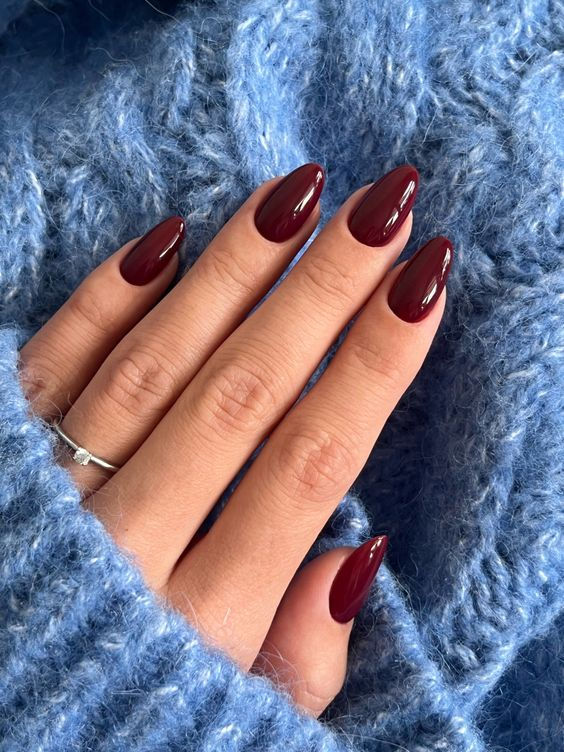 Burgundy Almond Nails: A Versatile Touch of Sophistication Against a Soft Blue Sweater.