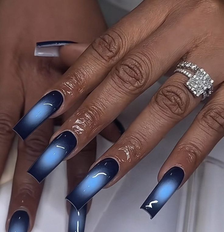 Stunning Ombre Nail Design: Deep Blue to Light with Elegant Long Tips and Glossy Finish, Complemented by a Gemstone Ring.