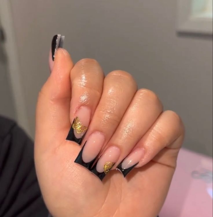 Chic French Tip Nail Design: Soft Nude with Bold Black Tips and Glamorous Gold Accents.