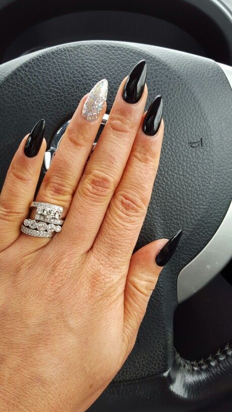 Edgy Elegance: Sleek Black Almond Nails with Glitter Accent and Chunky Silver Rings.