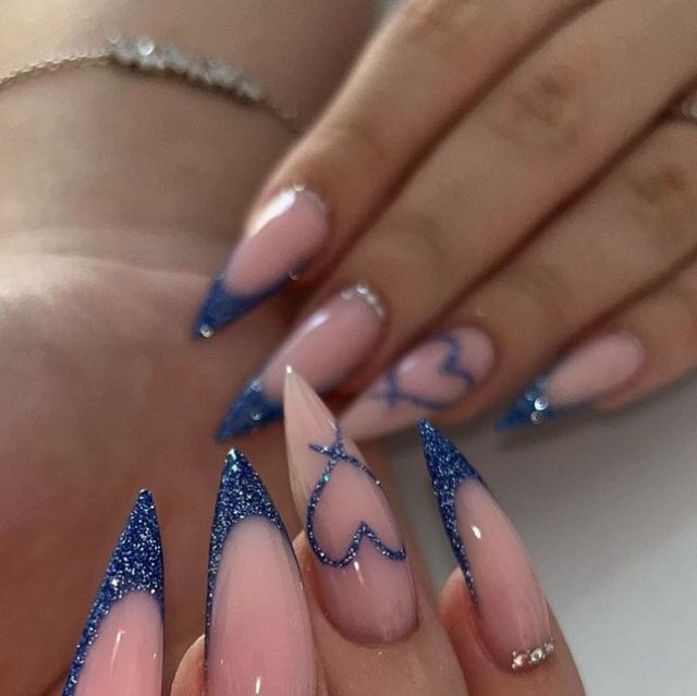 Chic Stiletto Nail Art: Vibrant Blue Glitter Tips and Playful Heart Motifs on Elegant Nude Base.