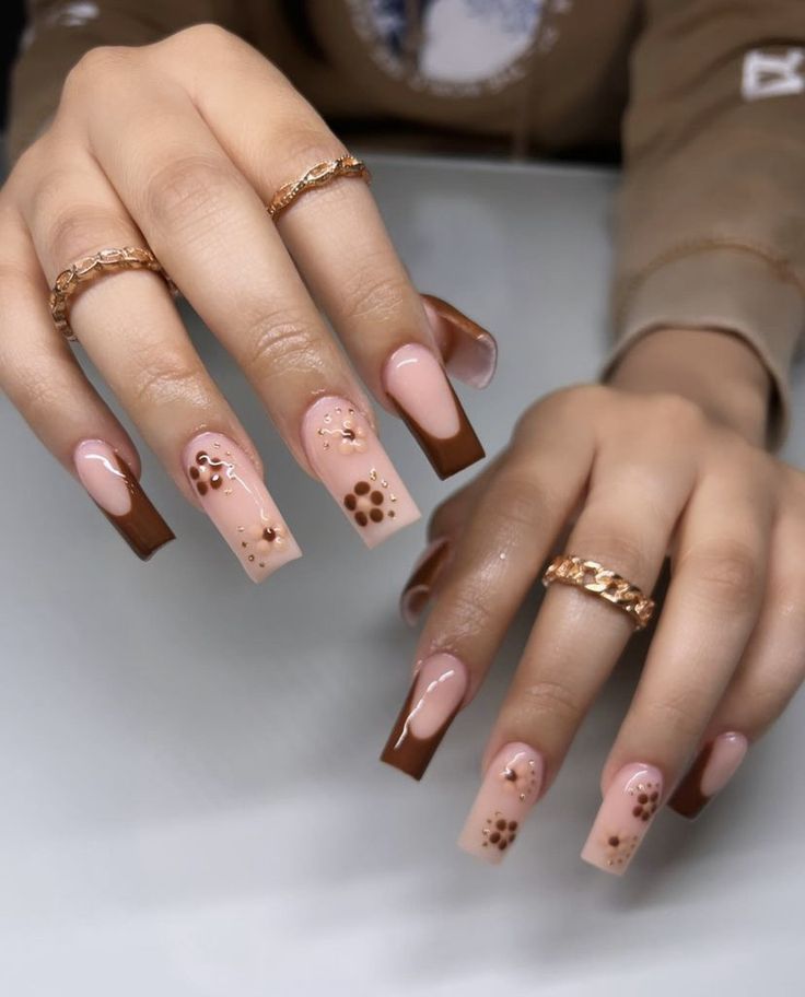 Sophisticated Nude and Brown Nail Design with Floral Patterns and Chic Rings.