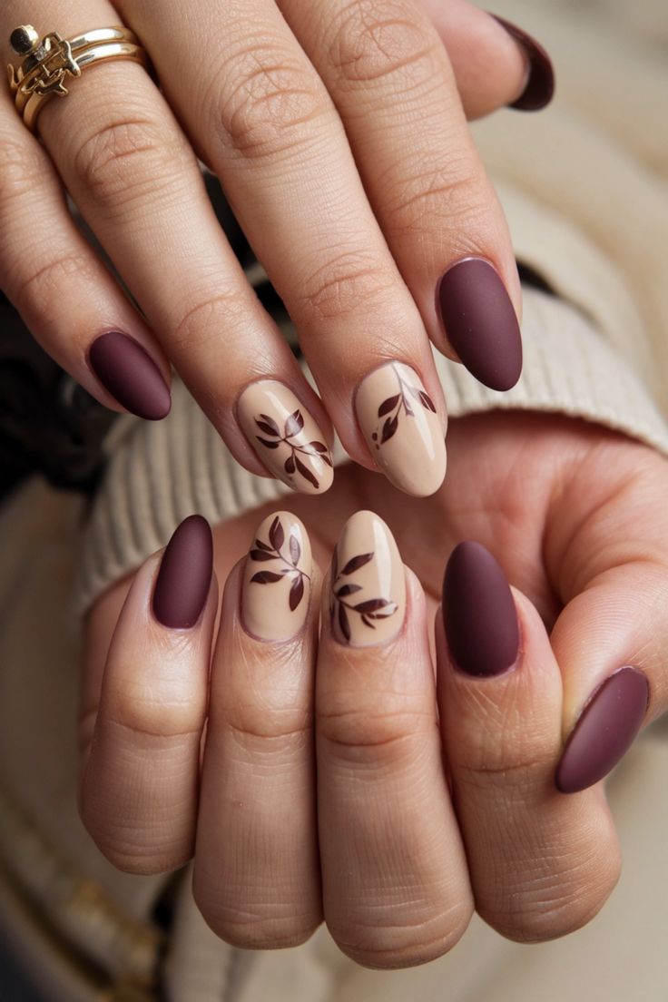 Sophisticated Nail Design: Deep Burgundy and Soft Neutrals with Elegant Leaf Motifs.