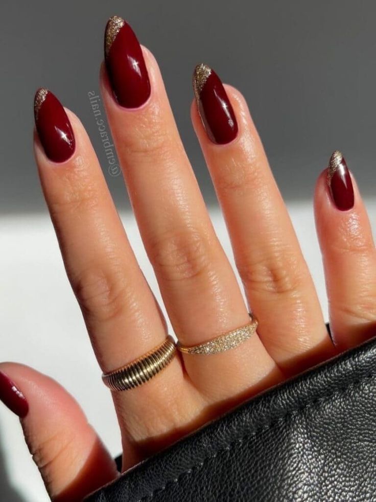 Sophisticated Deep Burgundy Nails with Shimmering Gold Accents and Elegant Rings.