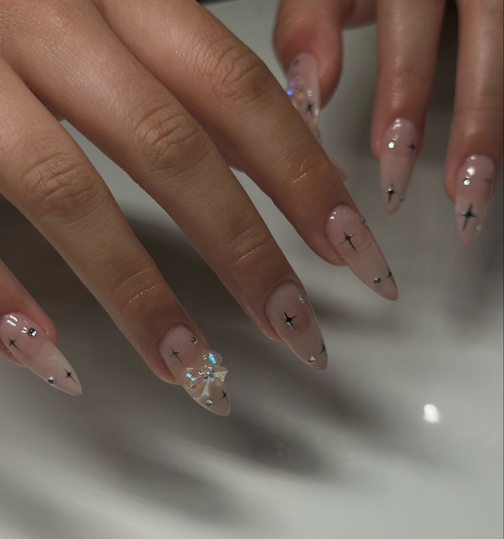 Sophisticated Almond-Shaped Nude Nails with Intricate Black Patterns and Crystal Embellishments.