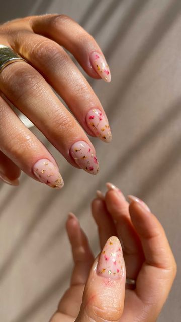 Chic Almond-Shaped Nails with Soft Nude Base and Playful Floral Glitter Accents.