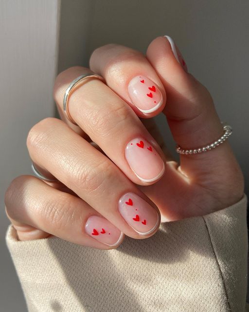 Charming Heart-Themed Nail Design with Whimsical Red Accents on a Soft Nude Base.