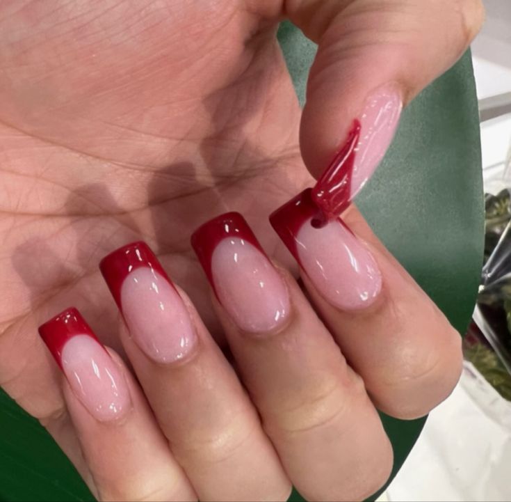 Chic French Tip Nail Design: Soft Nude Base with Bold Red Tips and Playful 3D Art.