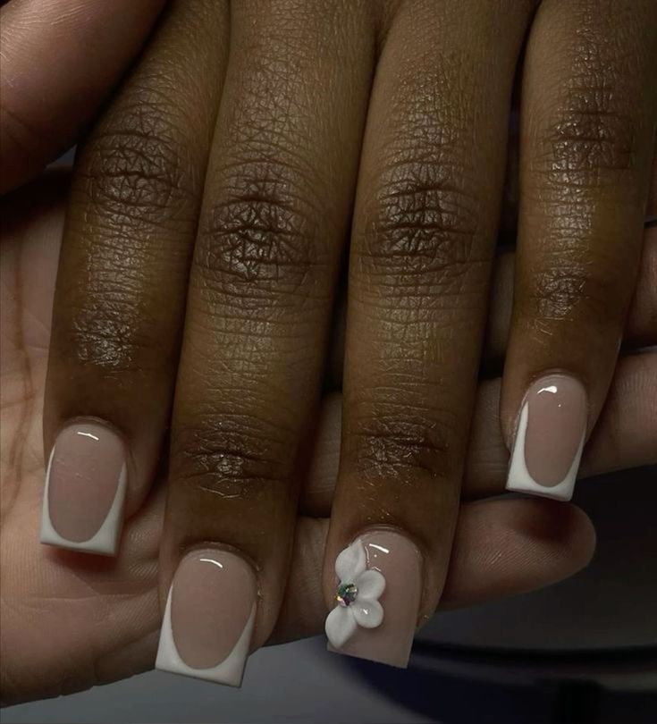 Chic Nude and White French Tip Manicure with Floral Accent and Gem Details.