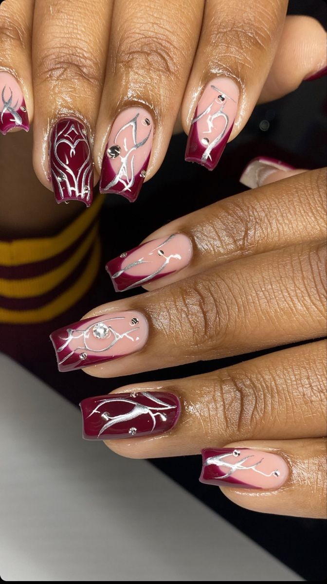 Sophisticated Nail Design Featuring Deep Burgundy, Soft Nude, and Intricate Silver Accents with Gemstone Highlights.