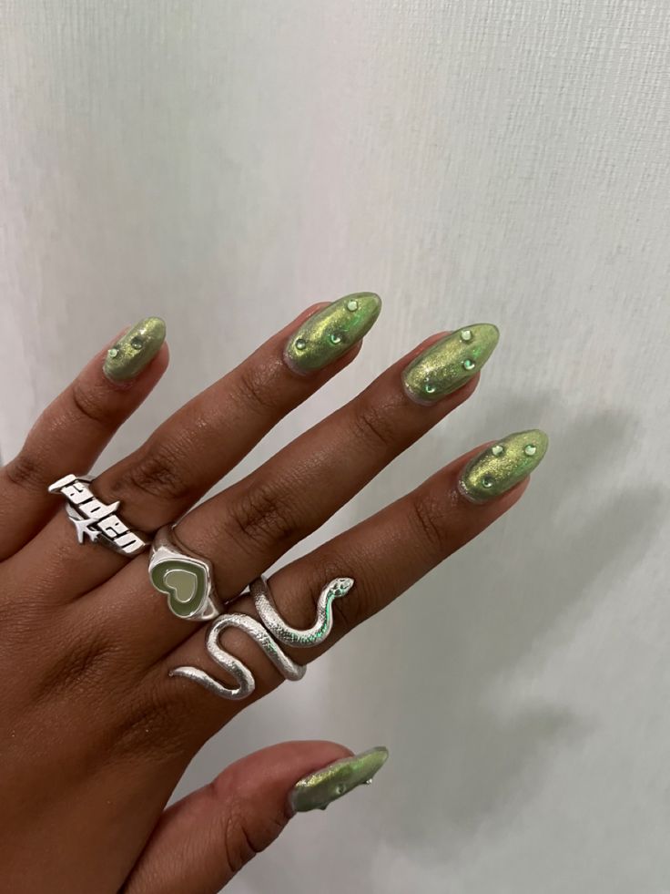 Trendy Shimmering Green Almond Nails with Gem Accents and Playful Rings.