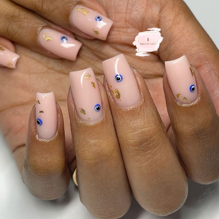 Chic Nude Nail Design with Golden Accents and Blue Eye Motifs.