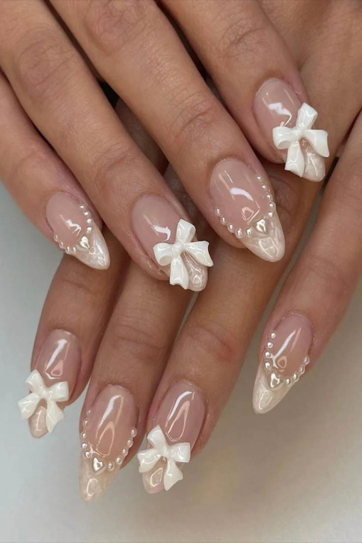 Chic Nude and White Nail Design with Romantic Bows and Pearl Accents.