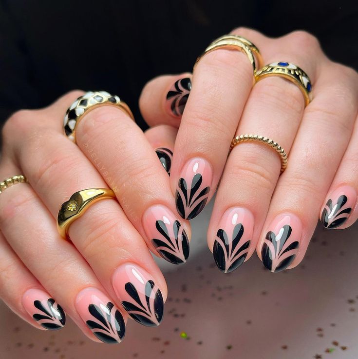 Chic Black and Nude Nail Design with Elegant Leaf Patterns and Delicate Rings.