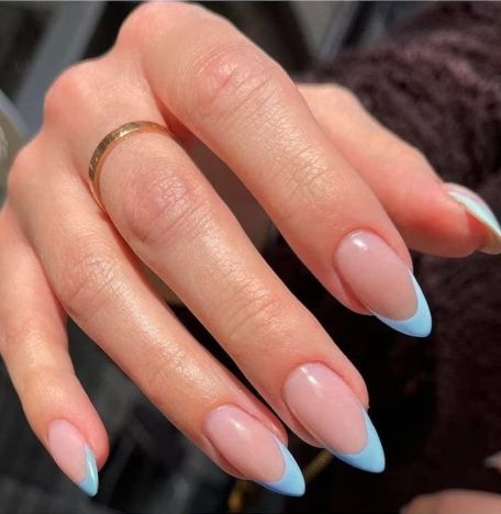 Chic Almond-Shaped Nails with Nude Base and Pastel Blue Tips, Complemented by a Simple Gold Ring.