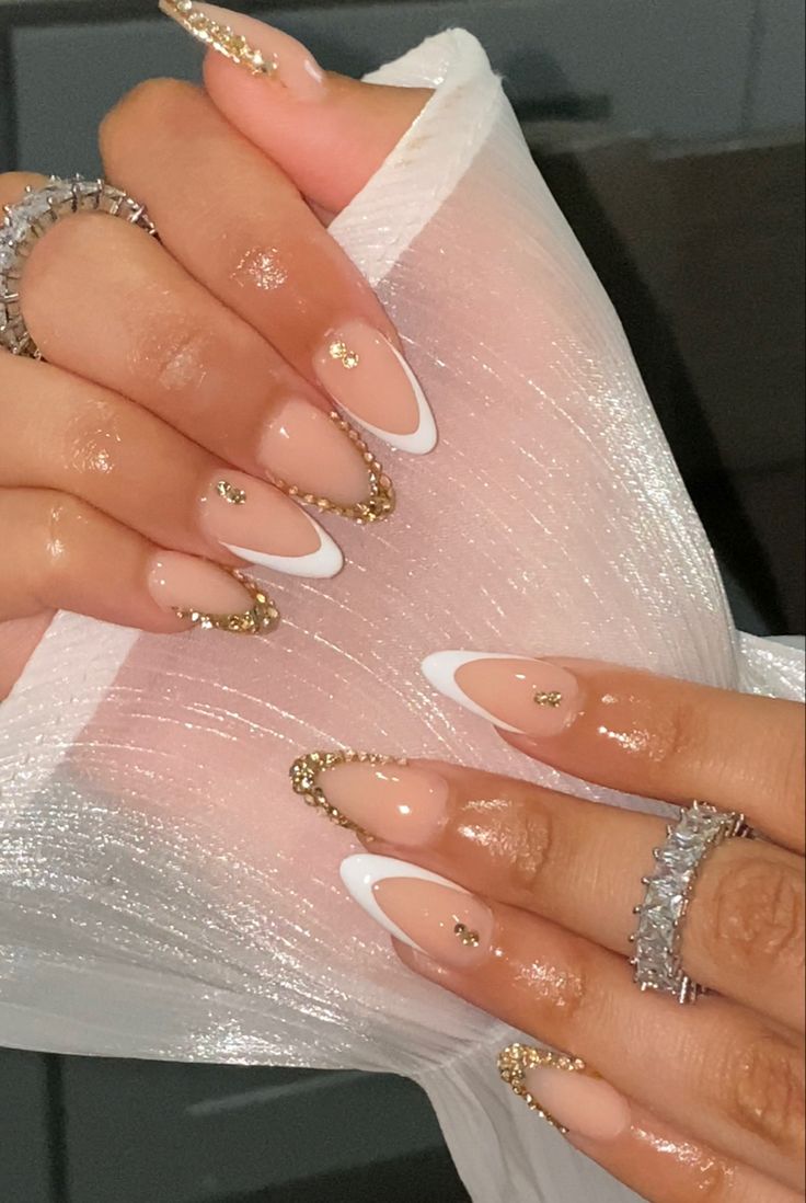 Chic Almond-Shaped Nails: Nude Base with Glamorous White Tips and Gold Accents.