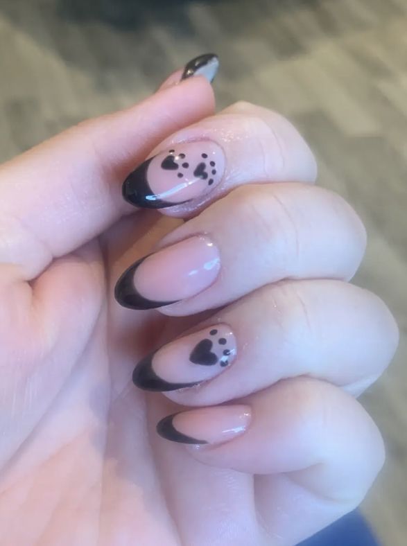 Sophisticated Almond-Shaped Nail Design with Nude and Black Colors, Heart Patterns, and Romantic Black Tips.