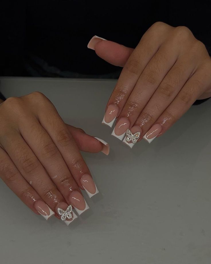 Glamorous French Tip Nail Design with Rhinestone Butterfly Accents on a Nude Base.