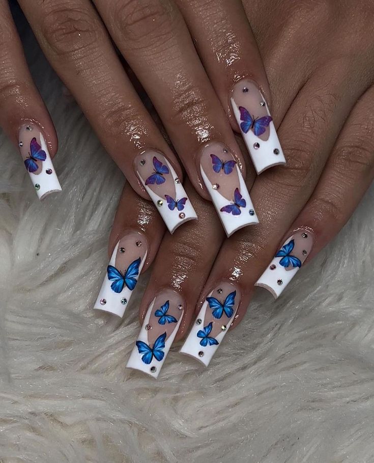 Elegant French-Tip Nail Design with Blue Butterflies and Sparkling Crystal Accents on Soft Pink Background.