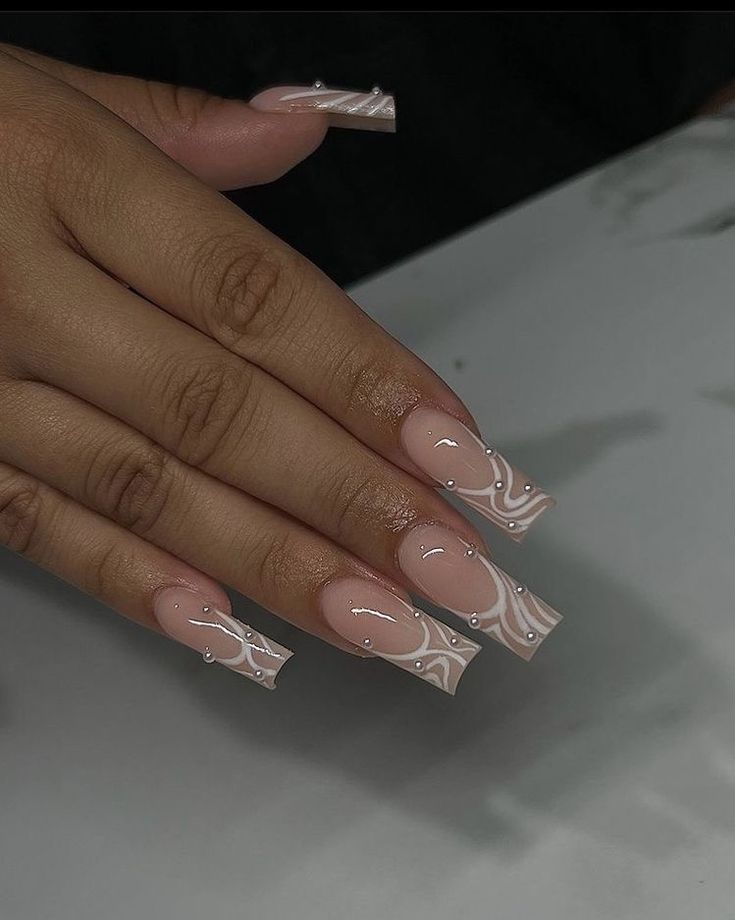 Elegant Soft Pink Nail Design with Swirled White Patterns and Rhinestones.