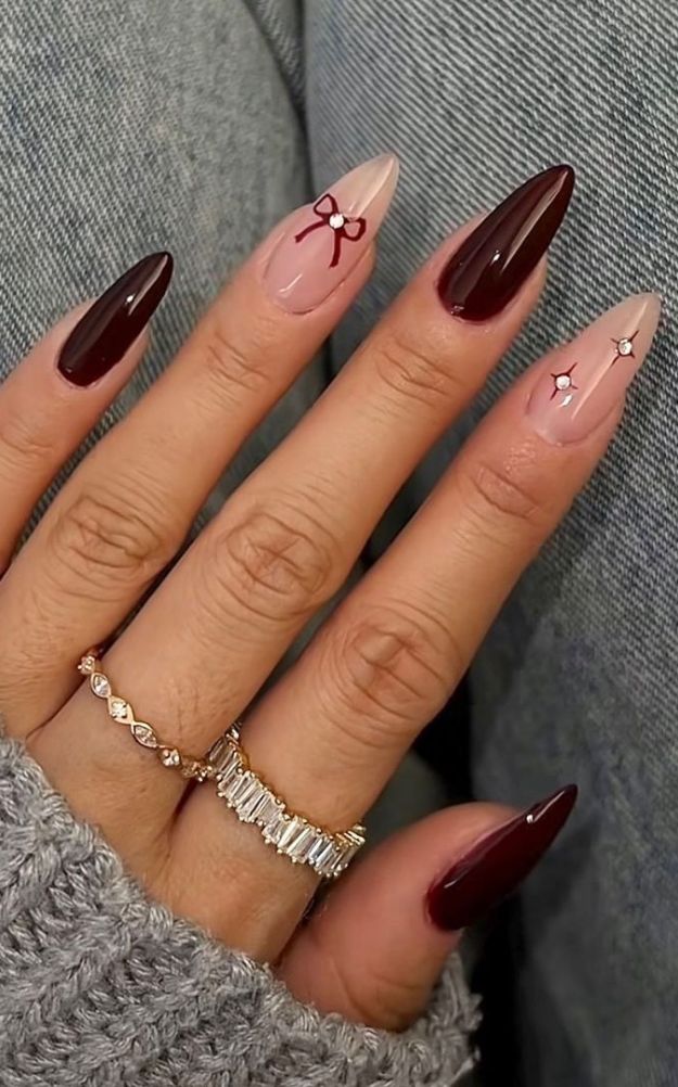 Chic Almond-Shaped Nail Design: Deep Burgundy and Soft Nude with Elegant Bows and Embellishments.