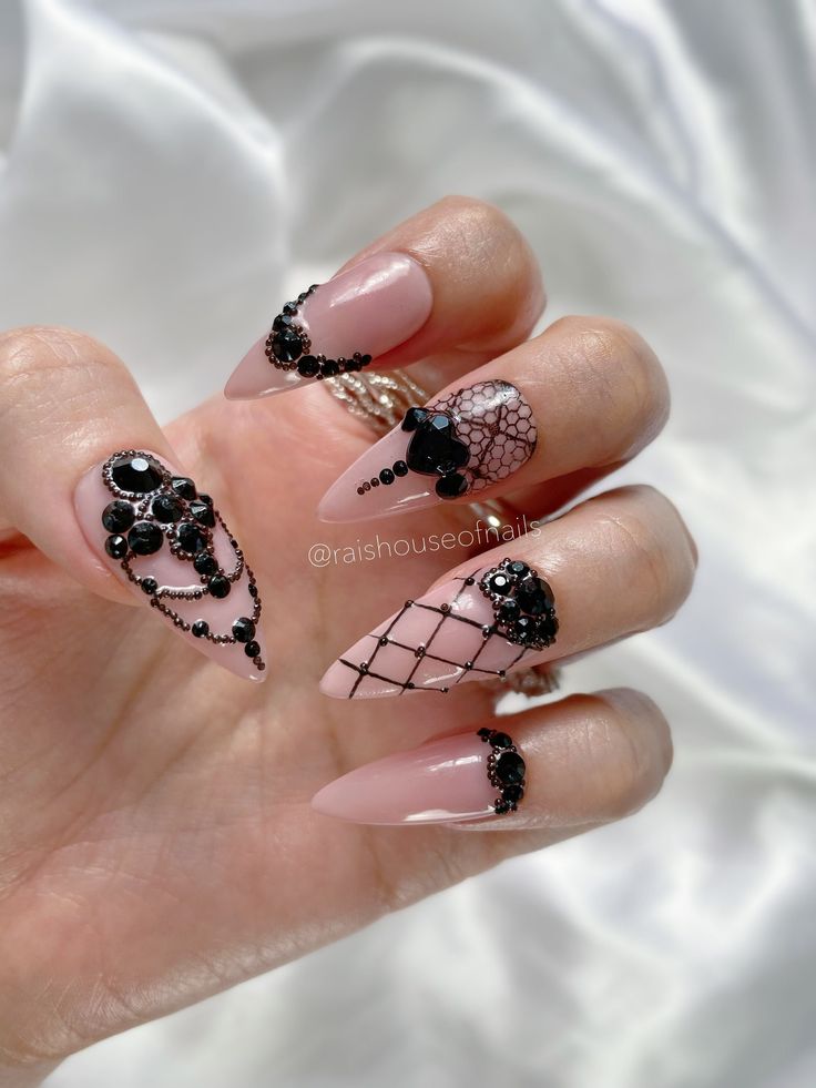 Sophisticated Nude and Black Nail Design with Intricate Lace Patterns and Gemstone Accents.