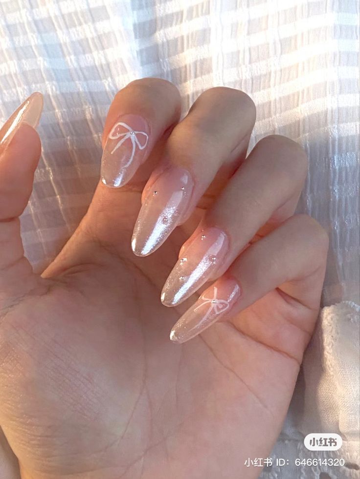 Chic Almond-Shaped Ombre Nail Design with Minimalistic White Bows and Shimmering Accents.