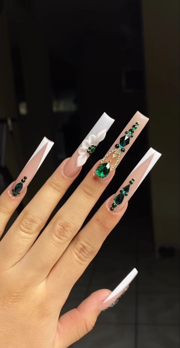 Chic Stiletto Nail Design: Nude Tones, White Accents, and Glamorous Green Gem Embellishments.