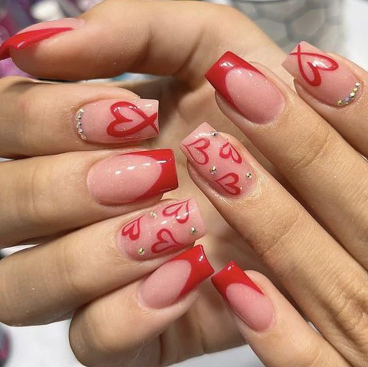 Romantic Red and Nude Nail Design with Heart Motifs and Sparkling Rhinestones.