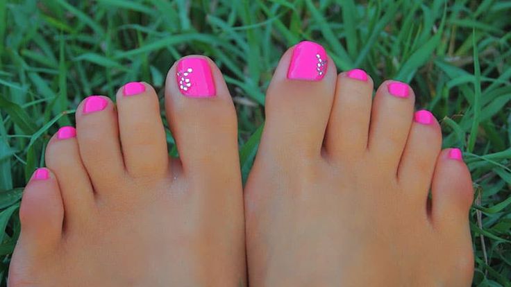 Vibrant Pink Pedicure with Rhinestones: A Playful Summer Statement Amidst Greenery.