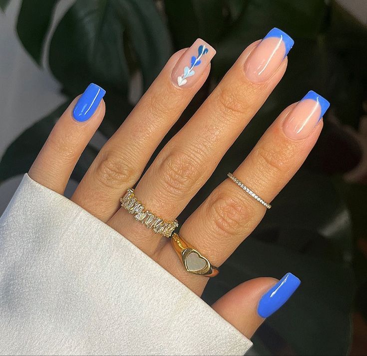 Vibrant Blue-Tipped Nails with Whimsical Floral Accent and Stylish Rings.