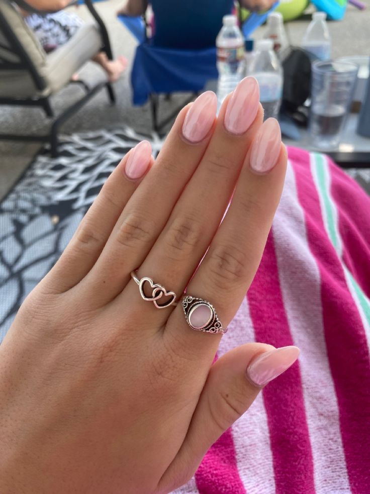 Chic Almond-Shaped Nails with Soft Pink Polish and Elegant Rings.