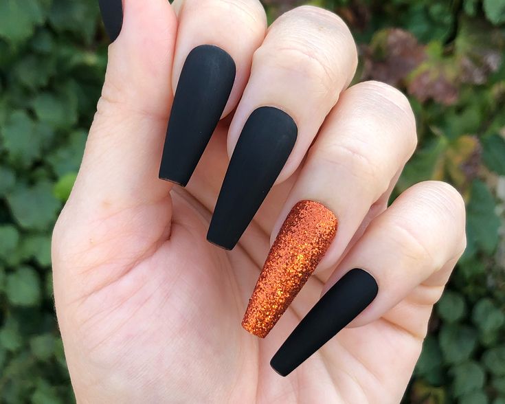 Bold Matte Black Nails with Glittery Orange Accent for a Striking Statement Look.