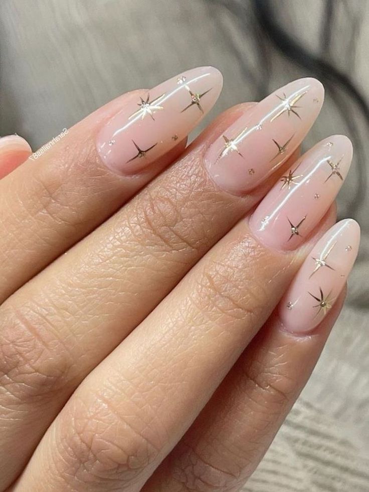 Sophisticated Almond-Shaped Nail Design with Soft Nude Base and Gold Star Accents.