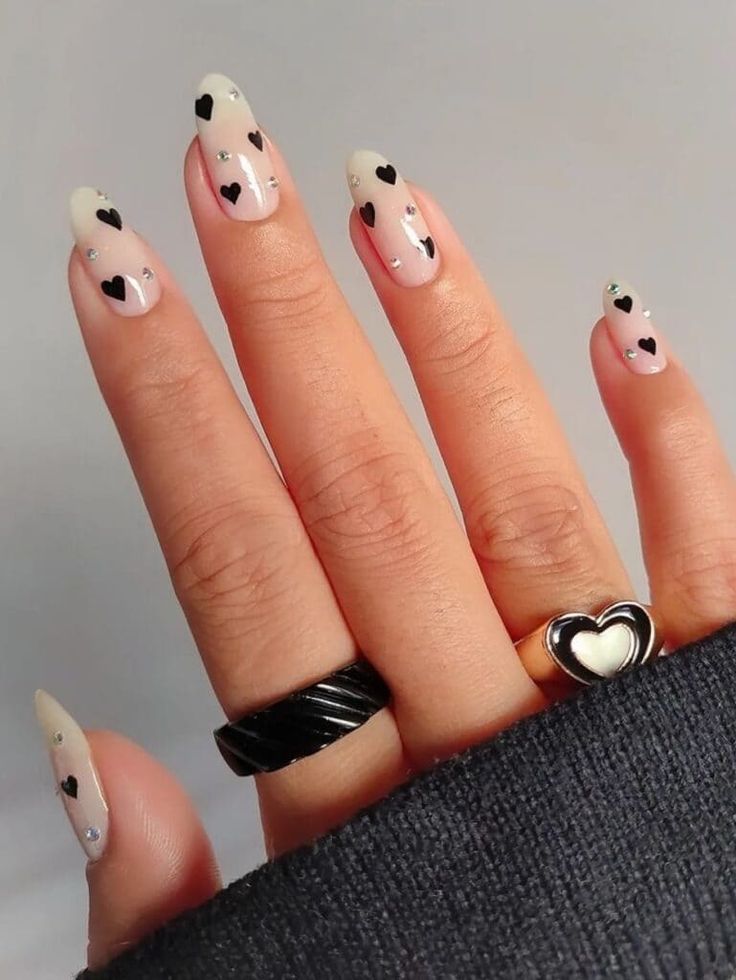 Elegant Chic Nail Design: Soft Nude and Light Pink with Black Hearts and Rhinestones.