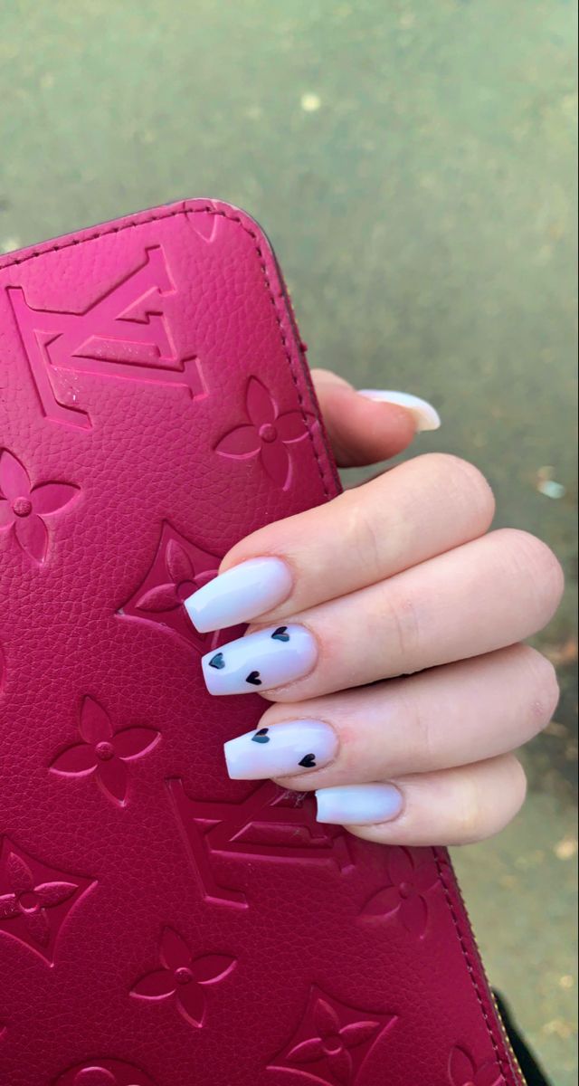 Chic manicure with soft white polish, black heart accents, and stylish pink wallet for a modern look.