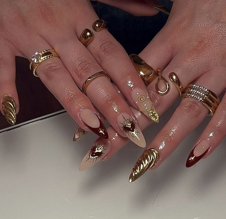 Sophisticated Nail Design with Neutral and Deep Red Tones Accented by Gold Details and Layered Rings.