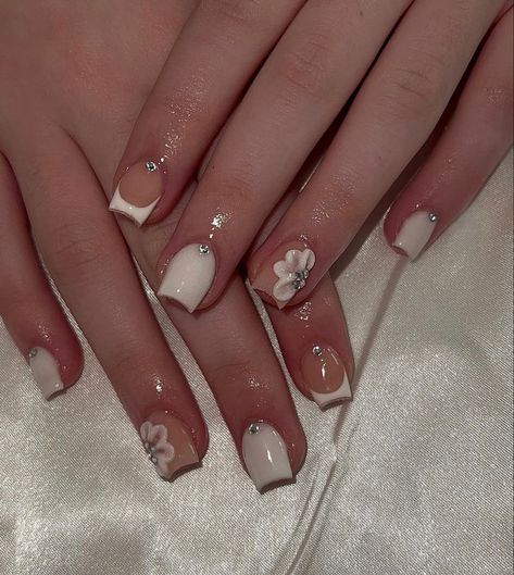 Sophisticated Nail Design: Soft White and Nude Palette with Floral Accents and Sparkling Rhinestones.