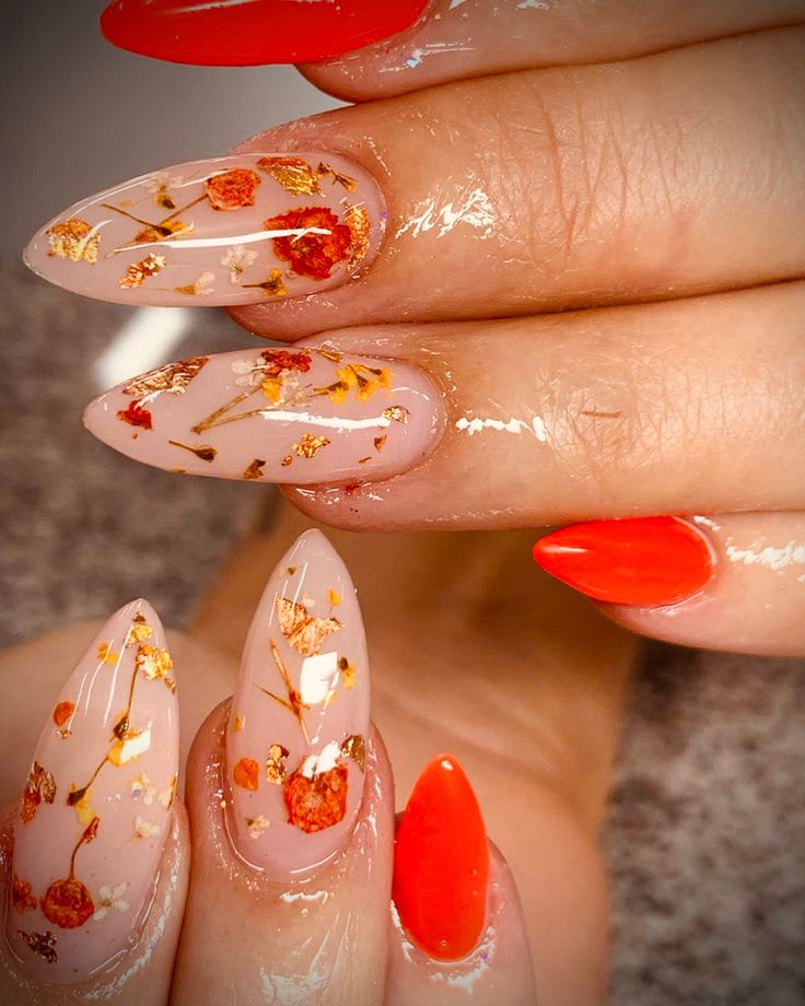 Elegant Floral Nail Design: Nude and Vibrant Reds with Gold Accents in Almond Shapes.